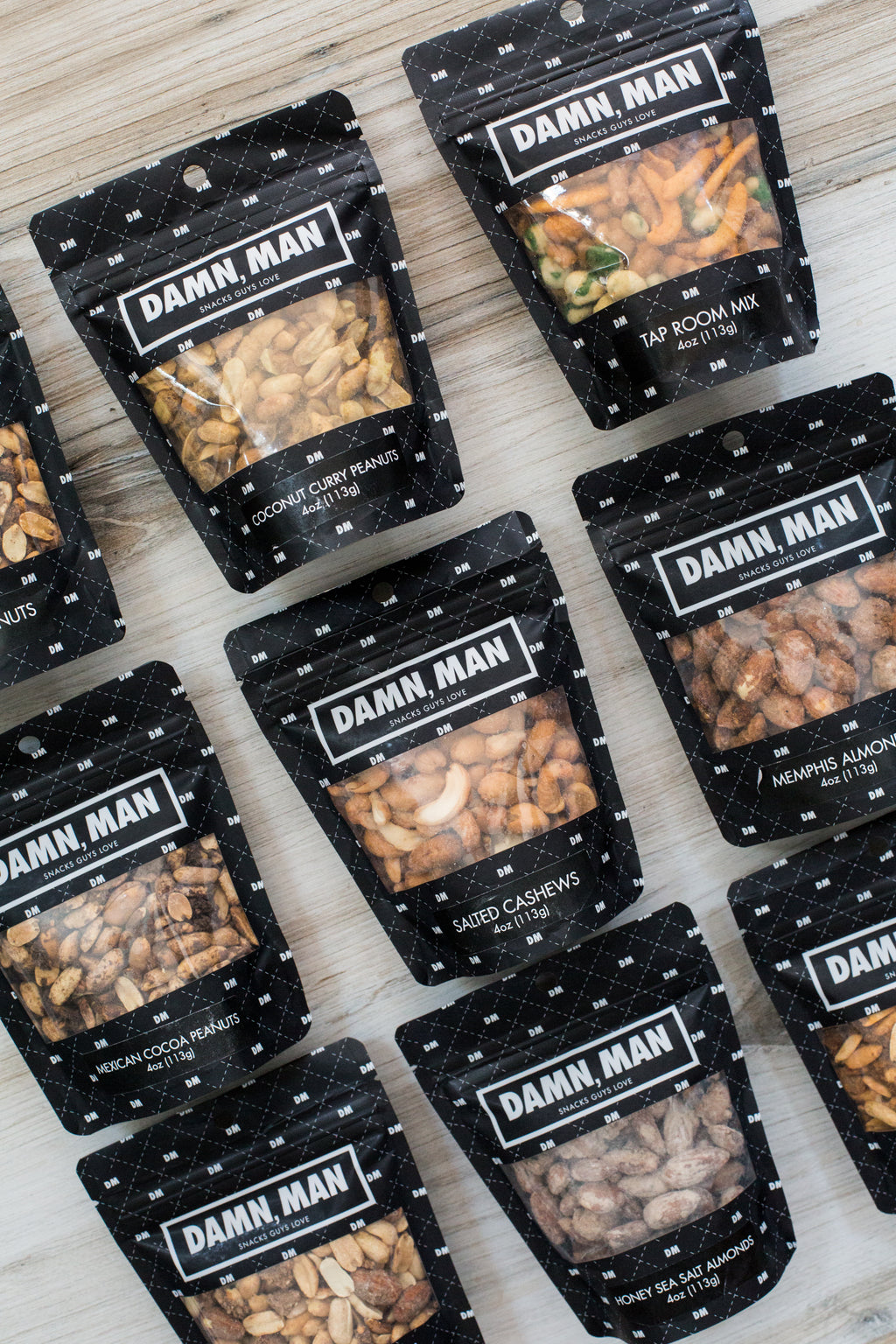 Build Your Own 6-Pack Box of Mixed Nuts by Damn, Man Gift Snacks laid out on a wooden surface.