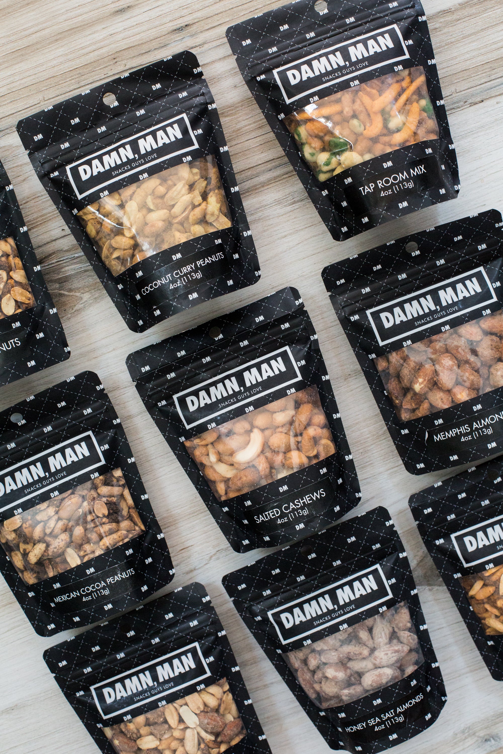 Build Your Own 6-Pack Box of Mixed Nuts by Damn, Man Gift Snacks laid out on a wooden surface.