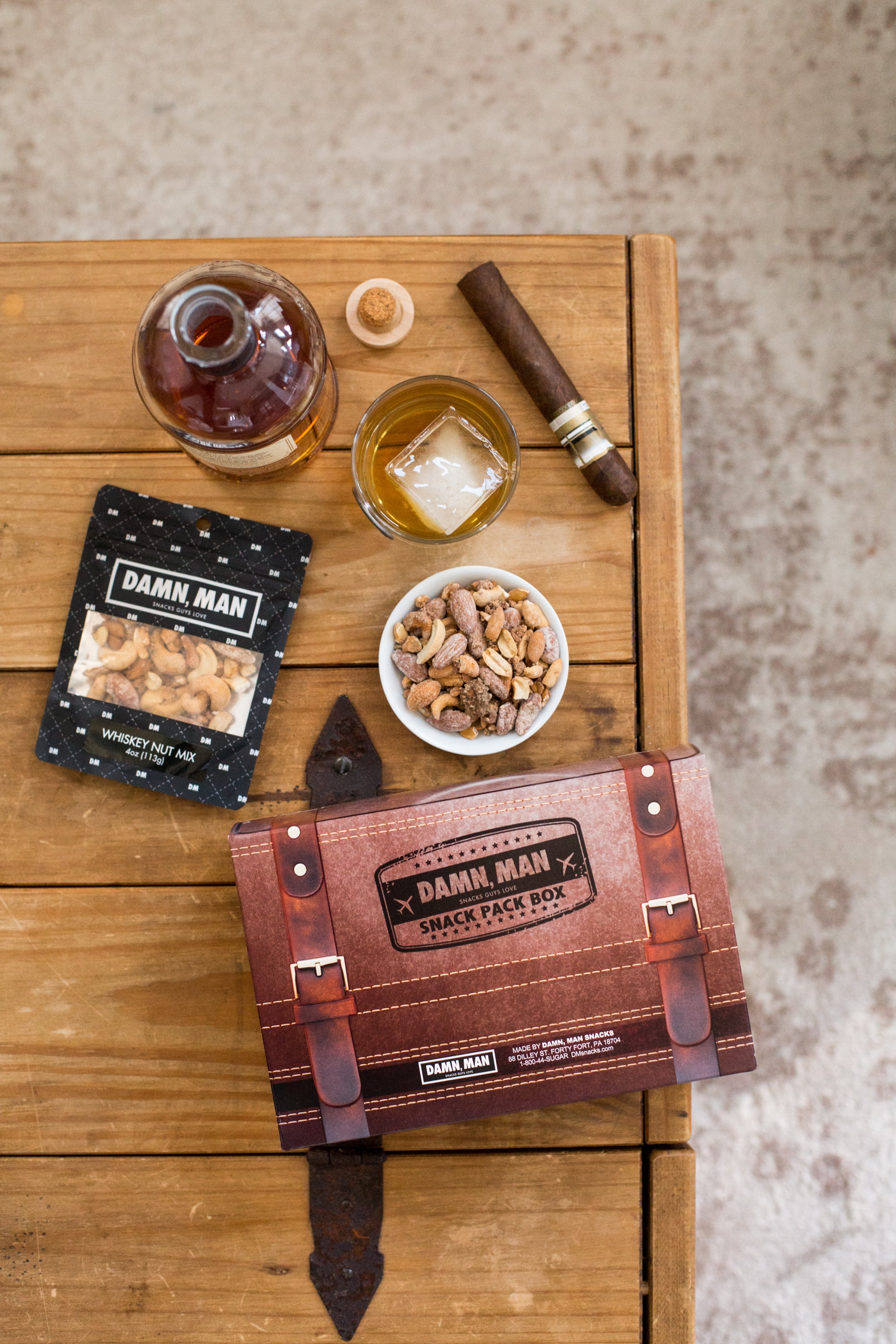 Build Your Own 4-Pack Box Mixed Nuts with whiskey, cigar, and snacks laid on a wooden table by Damn, Man Snacks.