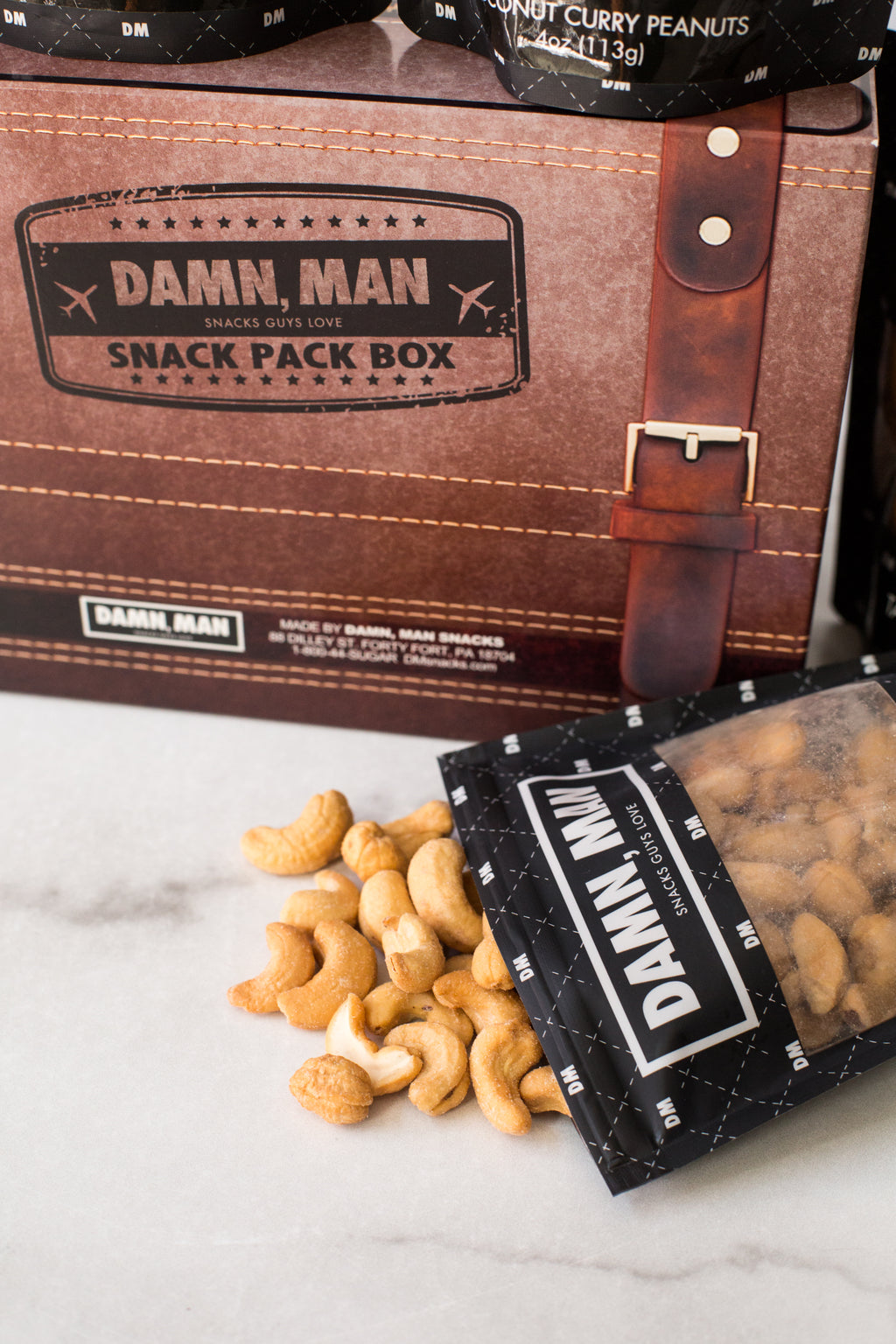 Damn, Man Snacks 4-Pack Box with Mixed Nuts spilling from a packet, perfect for customized snack adventures.