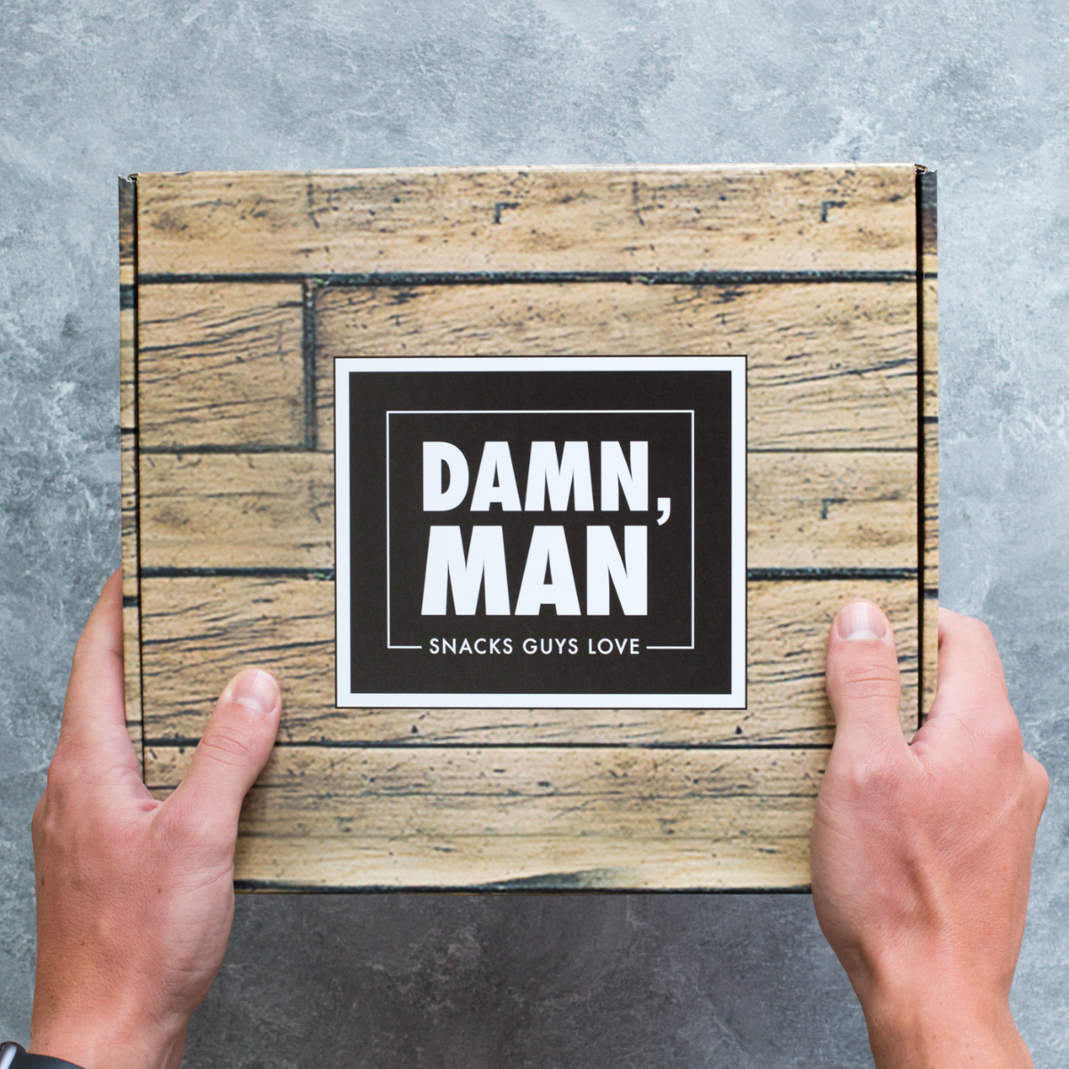 Hands holding Damn, Man gift box with gourmet snacks for men