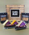Assorted snacks including cheese and sausages in front of a wood-look box with 'Damn, Man' branding.
