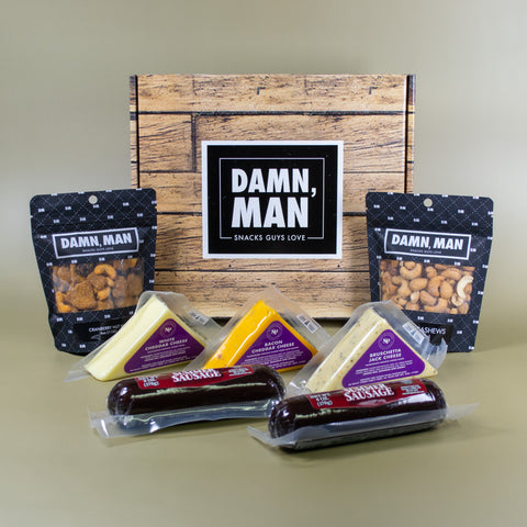 Assorted snacks including cheese and sausages in front of a wood-look box with 'Damn, Man' branding.