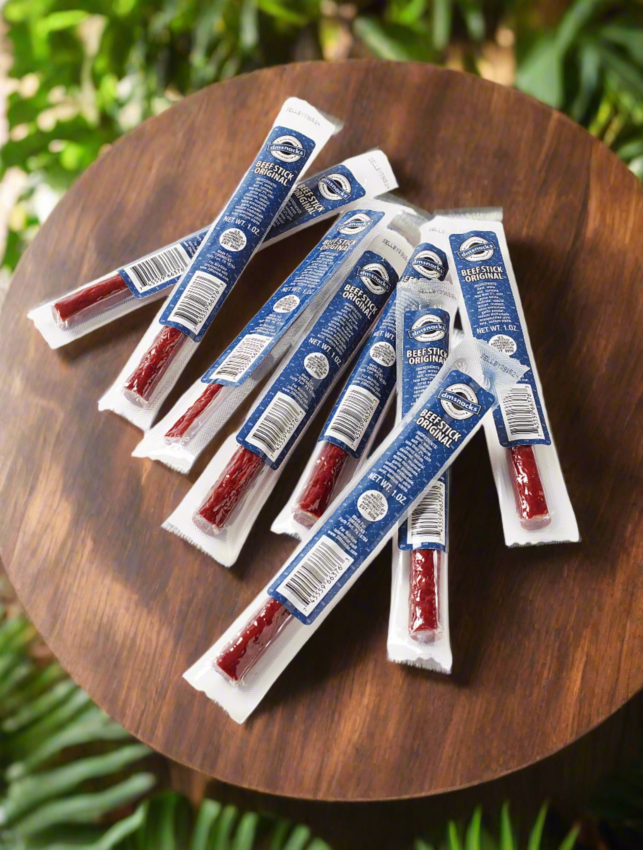 A collection of premium beef sticks from the Deluxe Beef & Brews Box arranged on a round wooden table, surrounded by greenery.