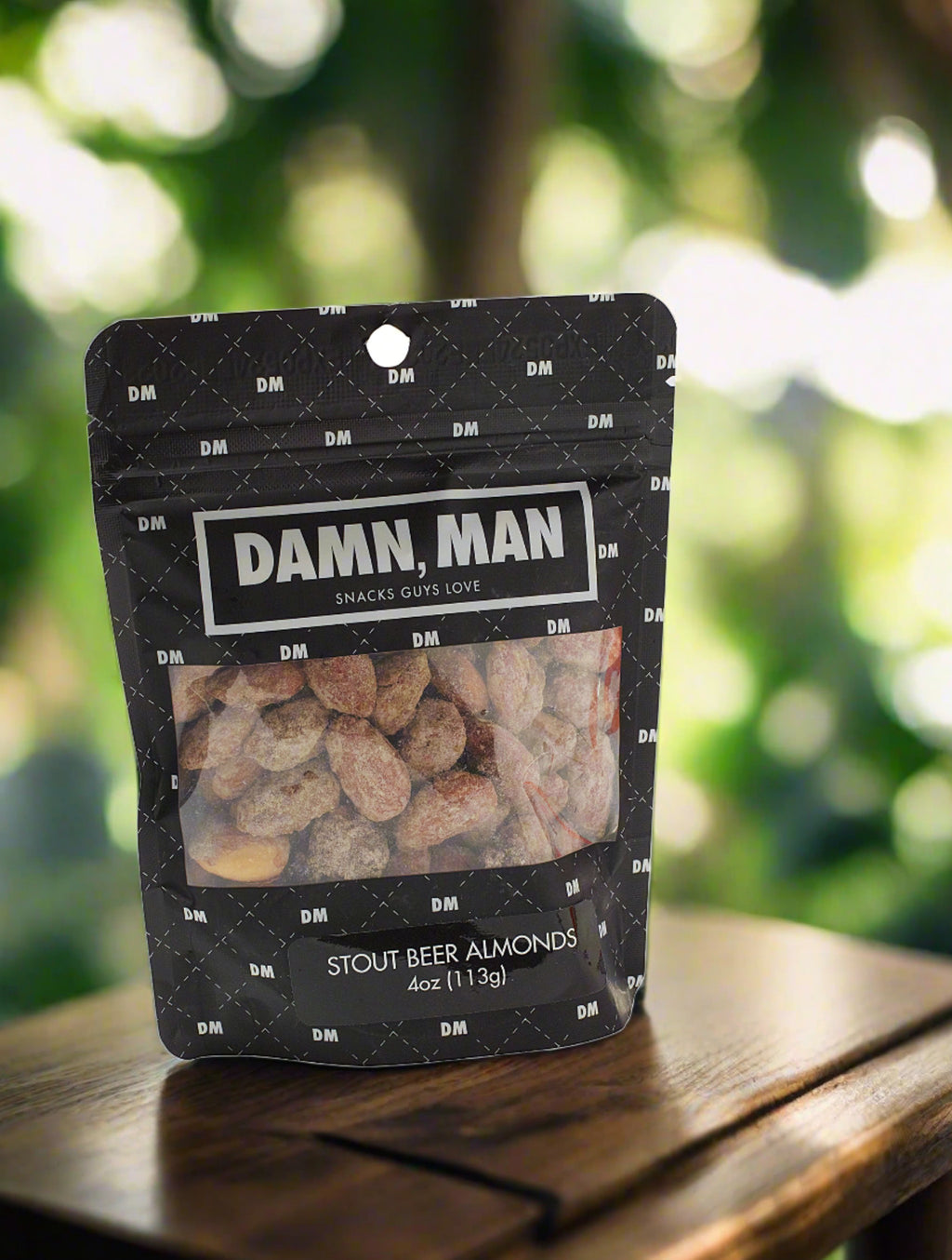 Snack pouch of Damn, Man Stout Beer Almonds on wooden surface with blurred greenery background