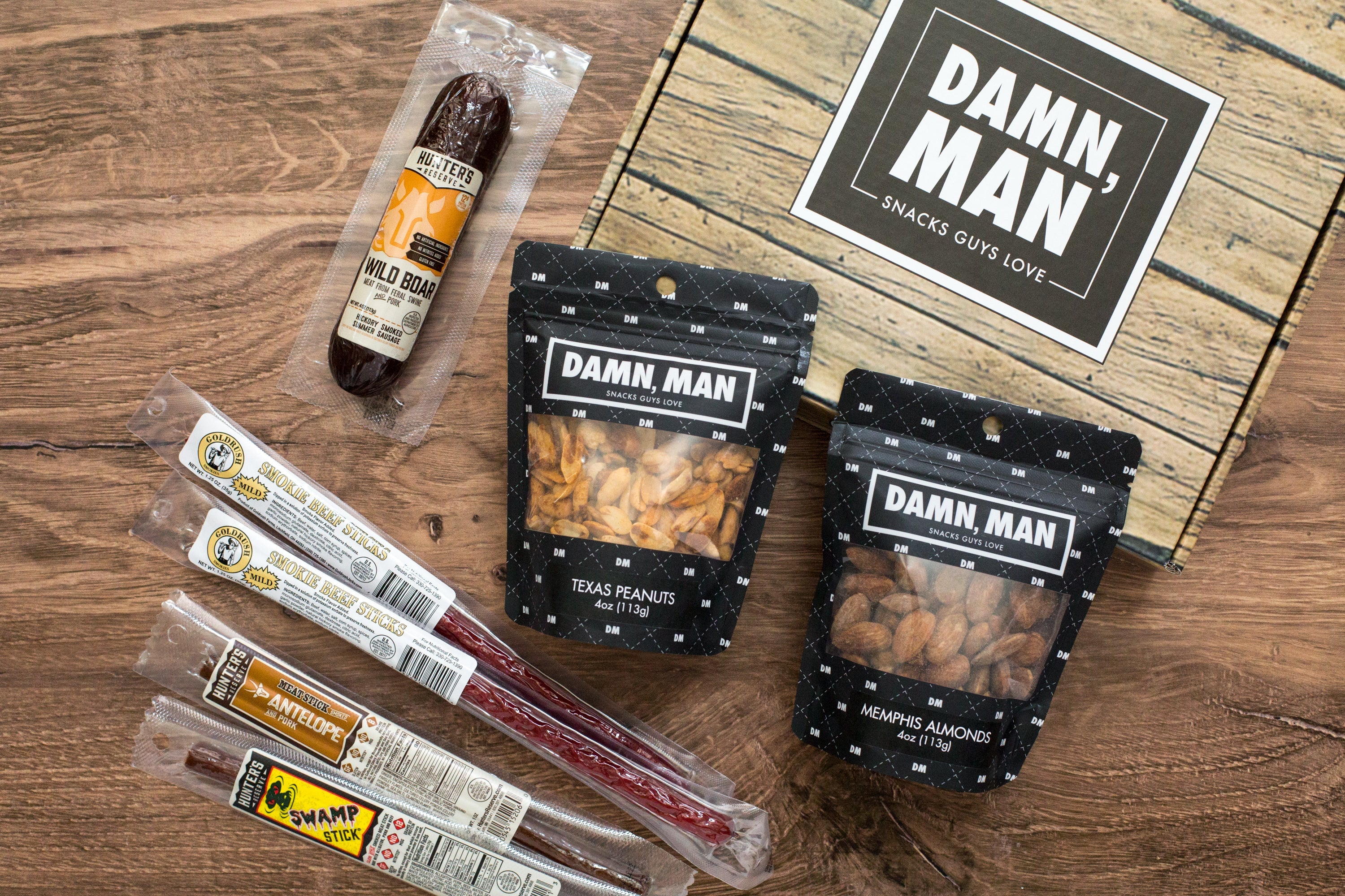 Nuts & Exotic Meats Box featuring Wild Boar Summer Sausage, Texas Peanuts, Memphis Almonds, and meat sticks from Damn Man Snacks.
